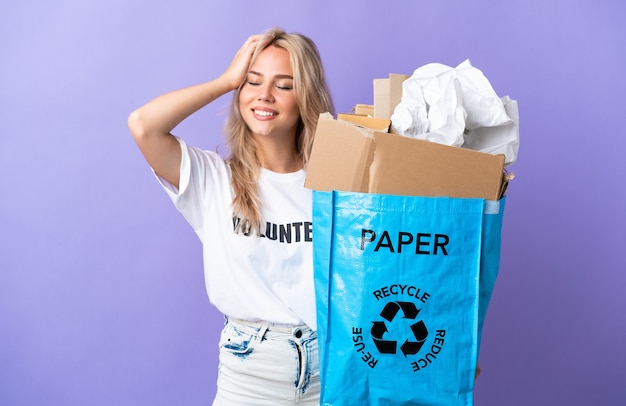 Joven rusa sosteniendo una bolsa de reciclaje llena de papel para reciclar aislado sobre fondo púrpura riendo