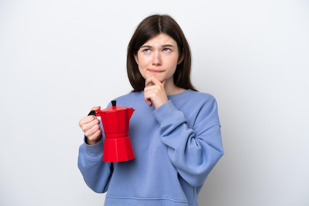 Joven rusa sosteniendo una cafetera aislada de fondo blanco con dudas y pensando