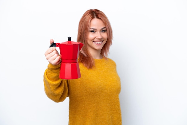 Joven rusa sosteniendo una cafetera aislada de fondo blanco con expresión feliz