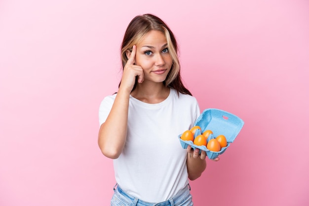 Foto joven rusa sosteniendo huevos aislados de fondo rosa pensando en una idea