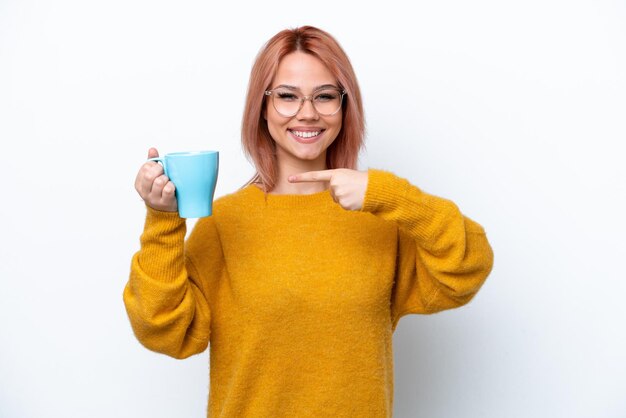 Joven rusa sosteniendo una taza de café aislada de fondo blanco y señalándola