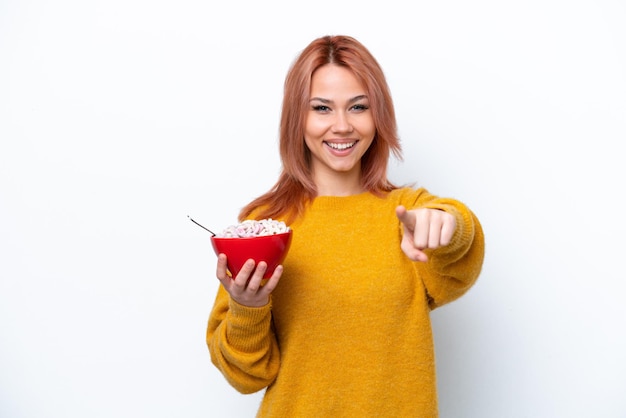 Una joven rusa sosteniendo un tazón de cereales aislado en un fondo blanco te señala con una expresión de confianza