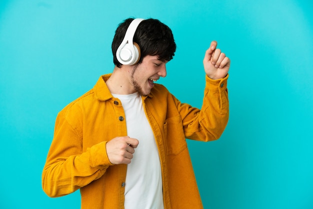 Joven ruso aislado sobre fondo azul escuchando música y bailando