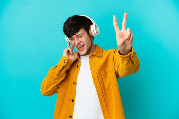 Joven ruso aislado sobre fondo azul escuchando música y cantando