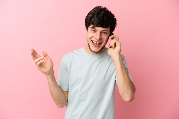 Joven ruso aislado sobre fondo rosa manteniendo una conversación con el teléfono móvil con alguien