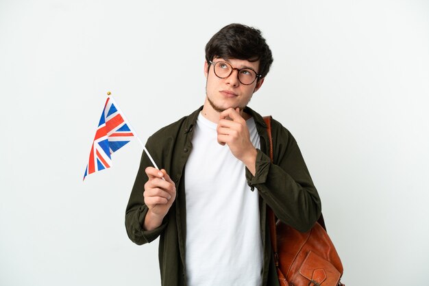 Joven ruso sosteniendo una bandera del Reino Unido aislado sobre fondo blanco y mirando hacia arriba