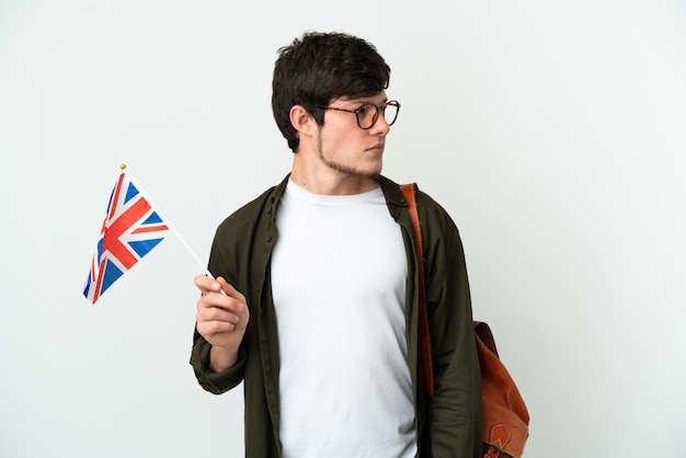 Joven ruso sosteniendo una bandera del Reino Unido aislado sobre fondo blanco mirando hacia el lado