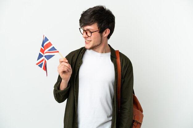 Joven ruso sosteniendo una bandera del Reino Unido aislado sobre fondo blanco mirando de lado