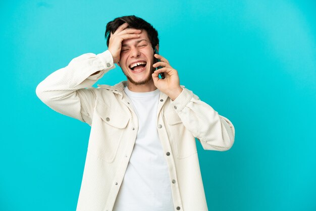 Joven ruso con teléfono móvil aislado sobre fondo azul sonriendo mucho