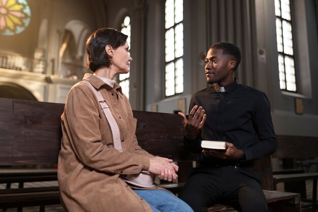 Joven sacerdote y mujer hablando en la iglesia mientras sostiene una biblia