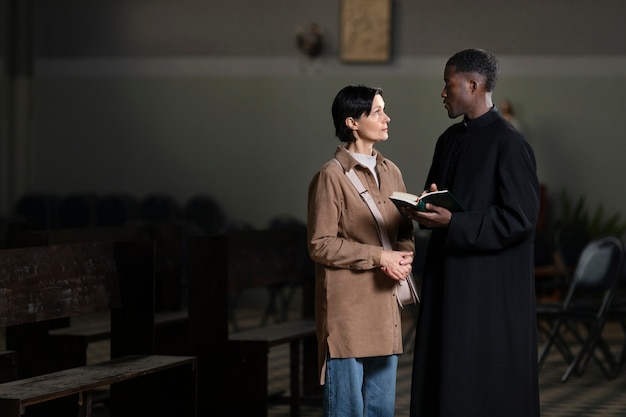 Joven sacerdote y mujer hablando en la iglesia mientras sostiene una biblia