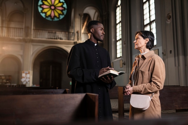 Foto joven sacerdote y mujer hablando en la iglesia mientras sostiene una biblia