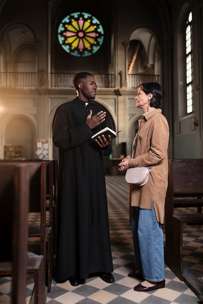 Foto joven sacerdote y mujer hablando en la iglesia mientras sostiene una biblia