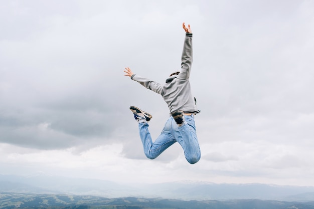 Joven saltando al aire libre sobre roca en las montañas cielo nubes