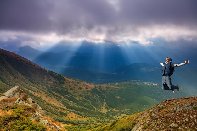 Joven saltando en la cima de una montaña contra el cielo