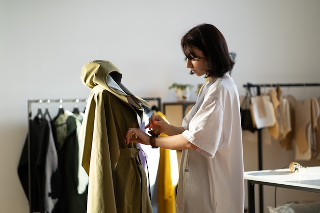 Joven sastre ajustar detalles de cuello al modelo de ropa en maniquí con agujas en estudio de moda