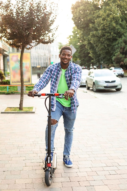 El joven con una scooter posa en la ciudad.