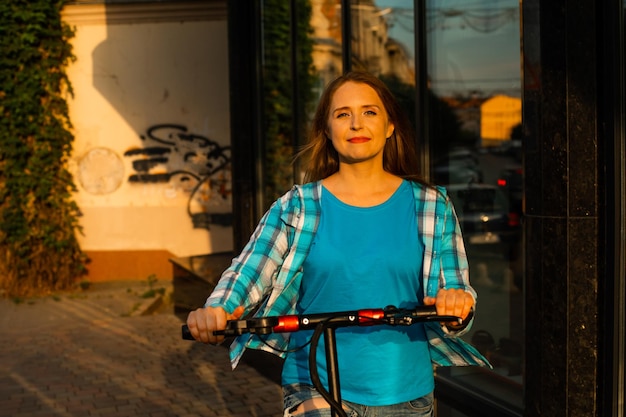 El joven con una scooter posa en la ciudad.