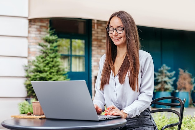 Una joven sentada en una mesa de café usa una computadora portátil y mira la pantalla