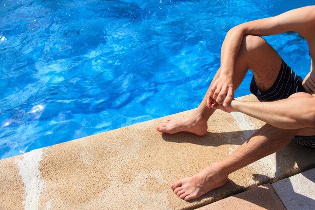 Joven sentado al borde de la piscina