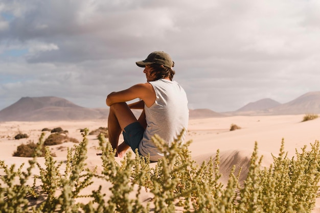 Joven sentado en la arena del desierto de las dunas de Corralejo en Fuerteventura