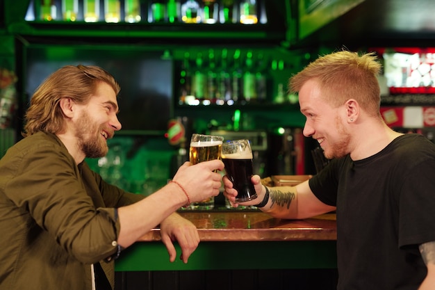 Joven sentado en la barra del bar y bebiendo cerveza junto con su amigo