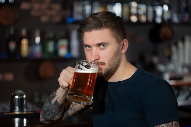 Joven sentado en la barra de bar con una pinta de cerveza light