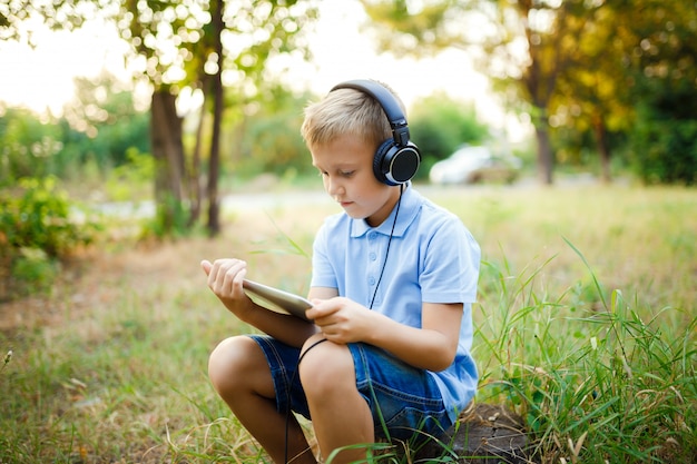 Joven sentado en el bosque con auriculares y un juego en tablet pc.