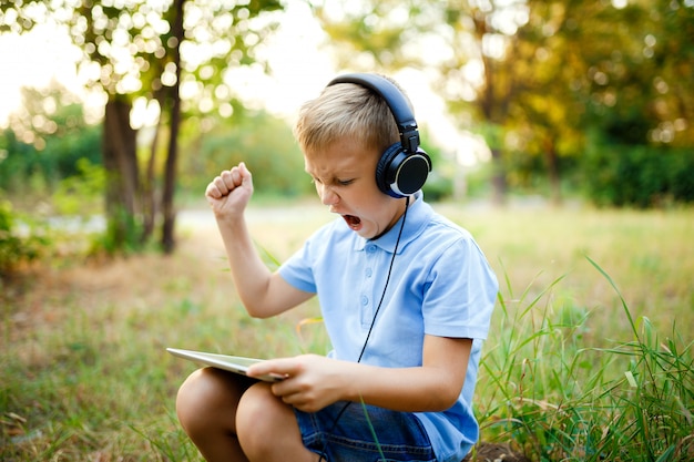 Joven sentado en el bosque con auriculares y un juego en tablet pc.