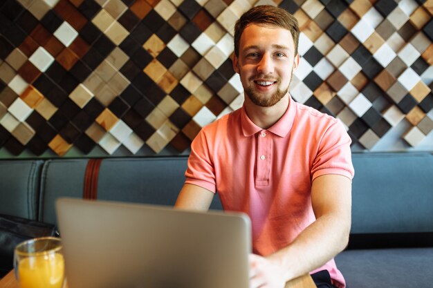 Un joven sentado en un café con una computadora portátil, trabajando, comprando en línea, hipster