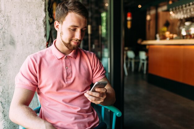 Joven sentado en la cafetería con computadora portátil y teléfono, trabajando, compras en línea, hipster