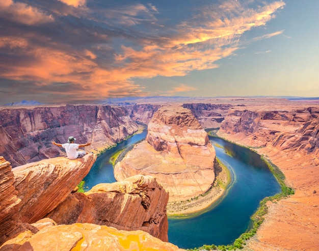 Un joven sentado con una camisa blanca y pantalón verde en Horseshoe Bend