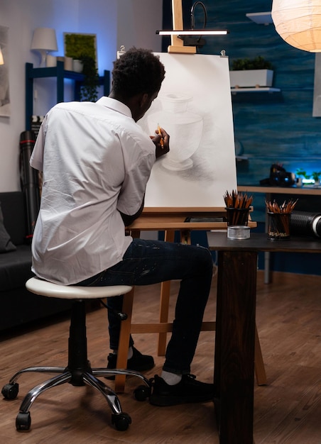 Joven sentado frente a un jarrón de dibujo de lienzo haciendo sombras con lápiz gráfico trabajando en un proyecto creativo durante la lección de arte. Artista estudiante pintando con herramientas profesionales de dibujo