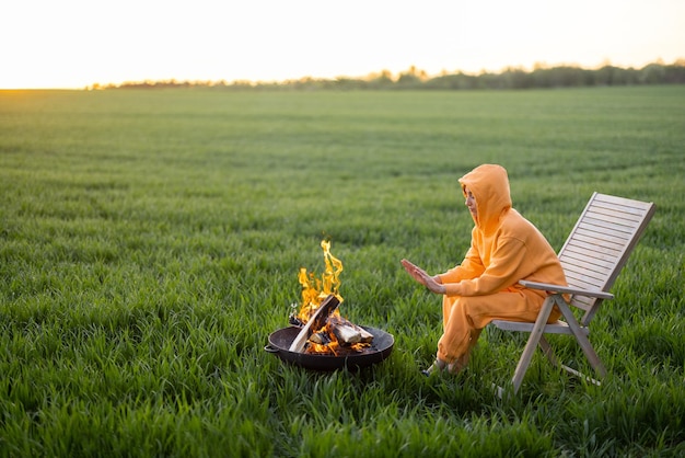 Joven sentado junto a la chimenea en campo verde al atardecer