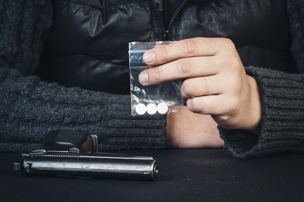 Joven sentado en la mesa con los brazos sosteniendo paquetes con drogas