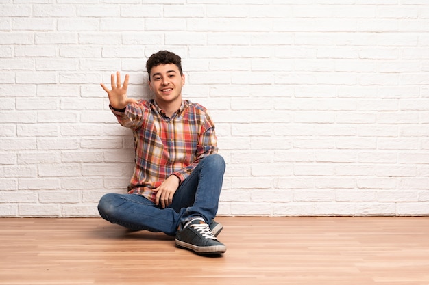 Joven sentado en el piso contando cinco con los dedos