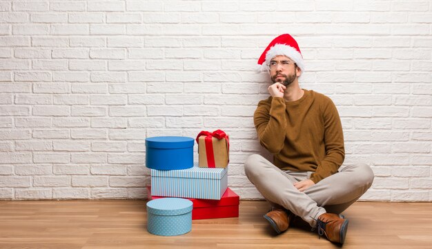 Joven sentado con regalos celebrando la Navidad dudando y confundido