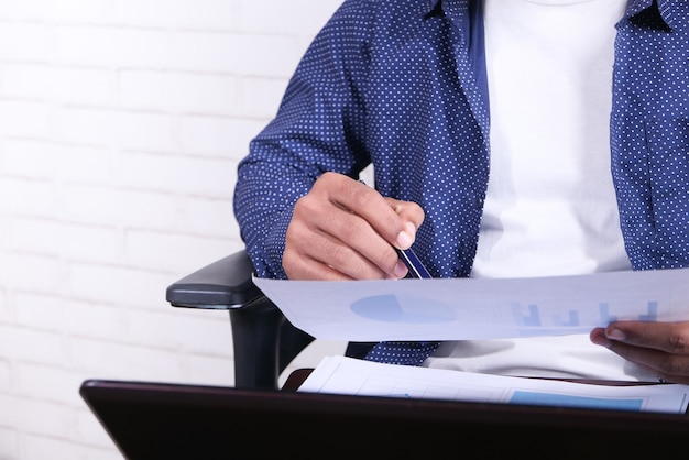 joven sentado en una silla analizando datos financieros en papel