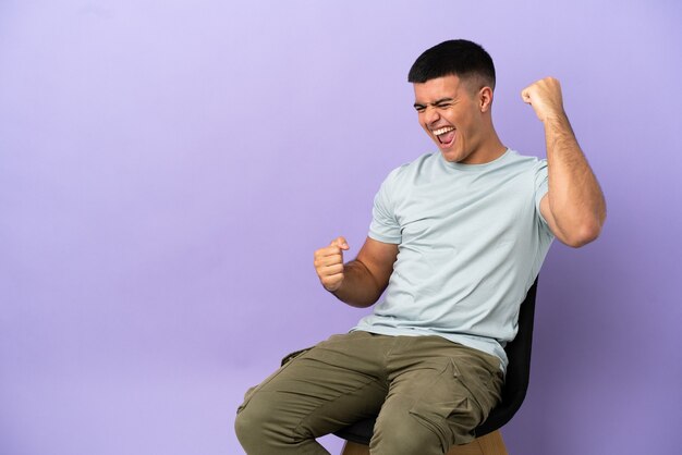 Foto joven sentado en una silla sobre antecedentes aislados celebrando una victoria