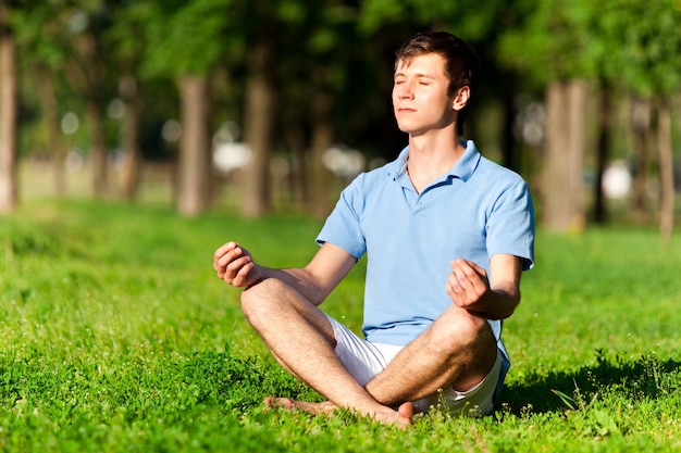 Joven sentado sobre la hierba verde y meditando