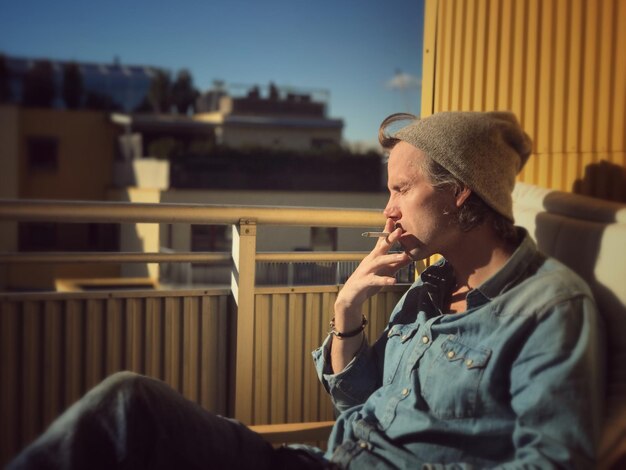 Foto joven sentado en el sol fumando