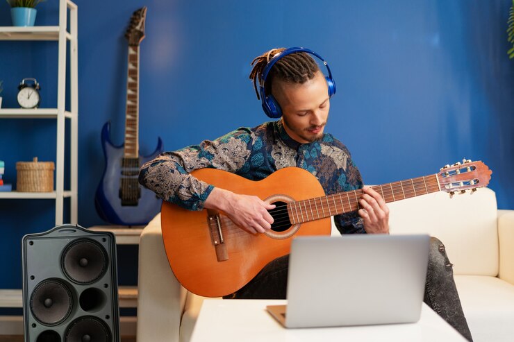 Foto joven sentado en su habitación y viendo tutorial de guitarra en la computadora portátil