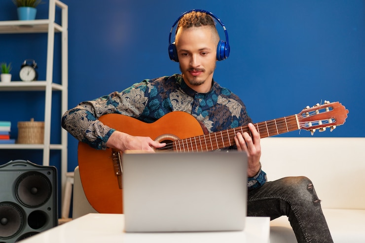 Foto joven sentado en su habitación y viendo tutorial de guitarra en la computadora portátil