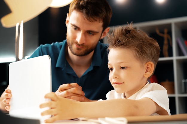 Joven sentado con su padre en la mesa y usando laptop