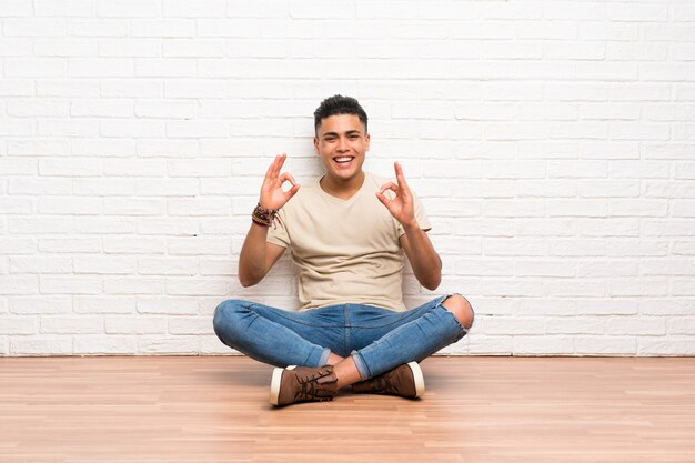 Joven sentado en el suelo mostrando un signo bien con los dedos