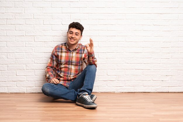 Joven sentado en el suelo mostrando signo ok con los dedos