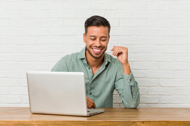 Joven sentado trabajando con su computadora portátil alegre riendo mucho