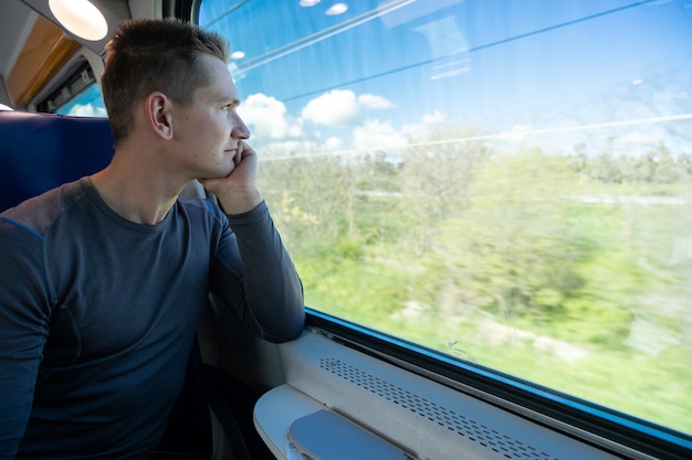 Joven sentado en el tren y mira por la ventana.