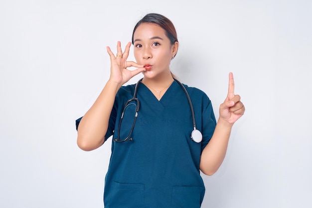 Una joven y seria enfermera asiática señala con el dedo hacia arriba y muestra un sello bucal que cierra los labios