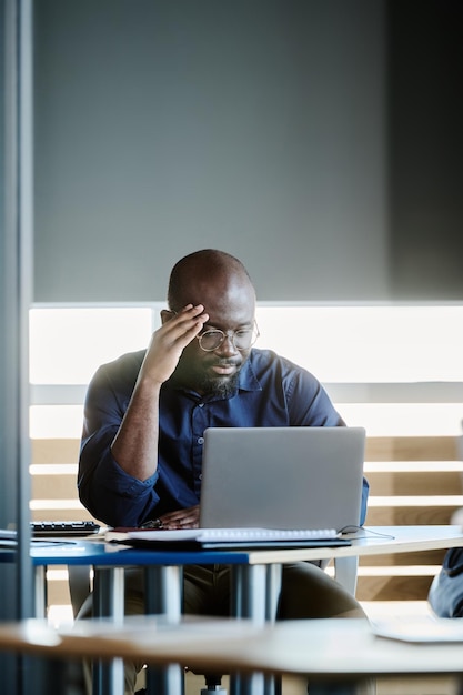 Un joven y serio director general afroamericano sentado frente a una laptop